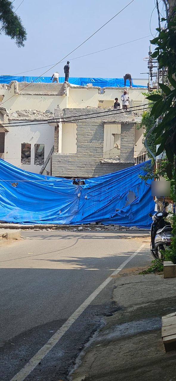 House being demolished behind a blue tarpaulin screen with workers on the roof